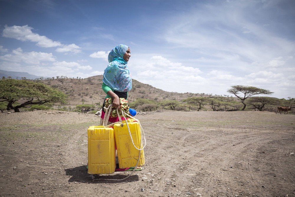 水を満たした容器を持って家路につく女性 / ©プラン・インターナショナル