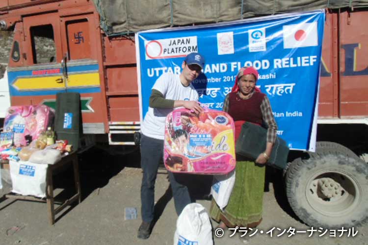 写真：インドの洪水被災者に支援物資を手渡す澤柳職員（左）