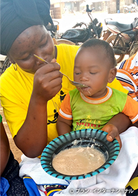 写真:栄養価の高いおかゆを子どもに与える母親（ギニア）