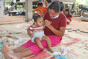 母親の膝でおかゆを食べる子ども / ©プラン・インターナショナル