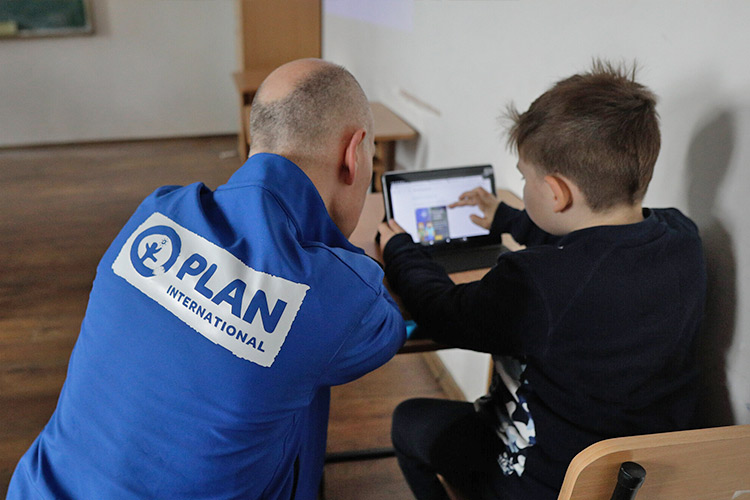 支給されたタブレットの操作をプラン職員から教わる男の子（ルーマニア） / ©プラン・インターナショナル