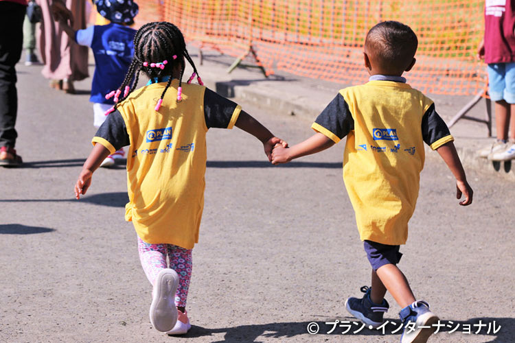 マラソン大会で手を取り合って走る女の子と男の子（エチオピア）