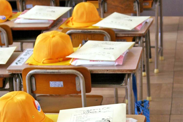 教室に整然と並んだ机の上の帽子と教科書