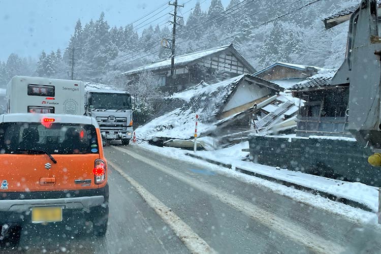 写真：雪のなか、輪島市に続く道路を進む。倒壊した家屋（右）
