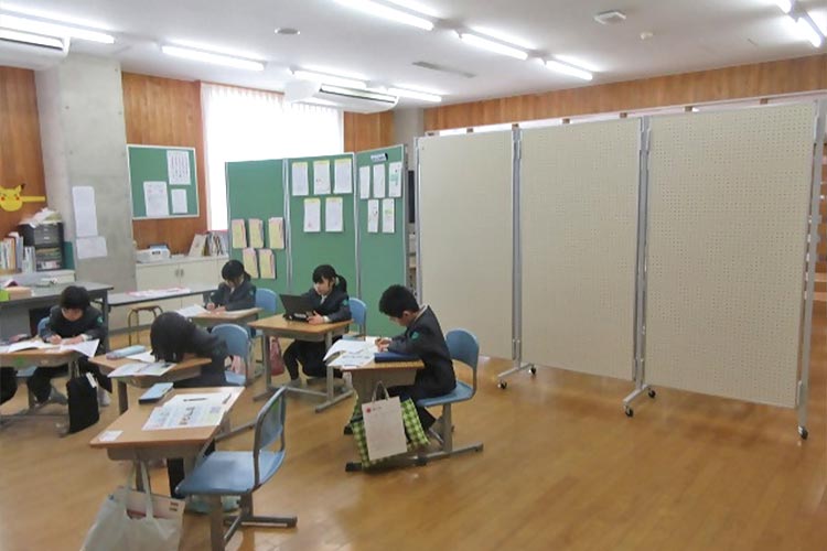 写真：基礎土台の損傷で校舎が使えない門前東・西小の児童が門前中学校の校舎内で学習。プランは可動式パーテーションを提供し、限られた空間で複数学年の授業を可能に