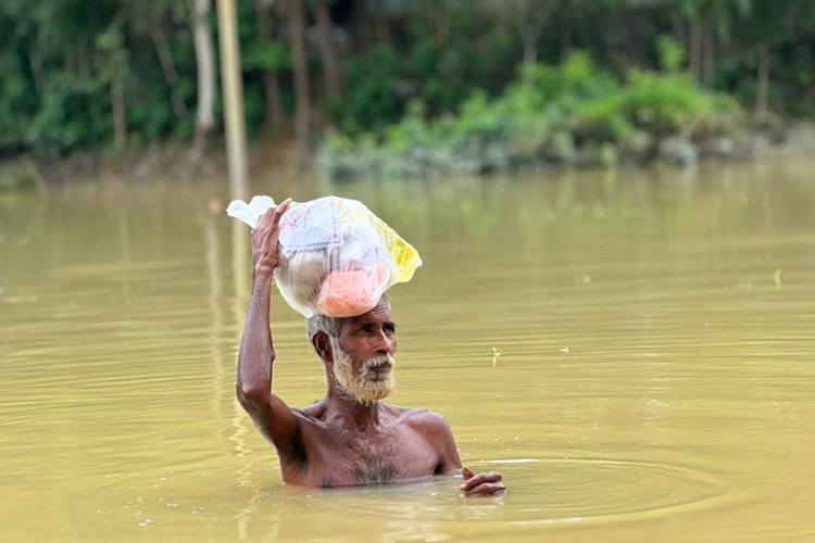 写真:冠水の中、最低限の荷物を持ち出し避難する住民