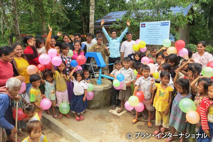 写真：落成式で、井戸の前に集まる村人たち。ひとみさんの名前の入った記念プレートも設置されている。