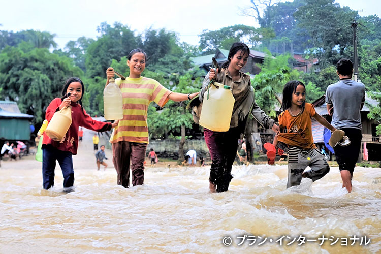 写真：浸水した交差点を水を持って横切る女の子たち